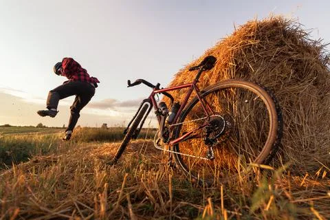 Happy cyclist jumping in a field with a haystack and a bicycle standing nearb Stock Photos