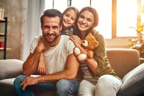 Happy dad and mom with their cute daughter and teddy bear hug and have fun si Stock Photos