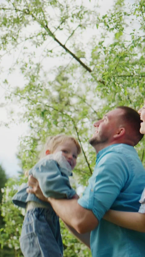 Happy dad throws toddler into air amid green trees 스톡 동영상 342396127