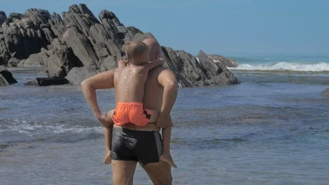 Happy daddy walks with boy on back along empty ocean beach Vidéo 115302354