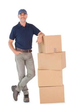 Happy delivery man leaning on pile of cardboard boxes Stock Photos