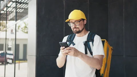 Happy delivery man writes text messages on his smartphone. On his shoulders and Stock Footage 172327880