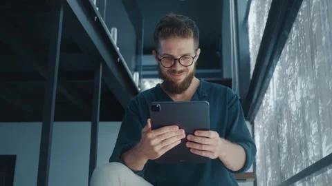 Happy Digital Marketer with beard and glasses using digital tablet while sitting Stock Footage 312120647
