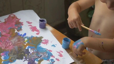 Happy dirty child drawing at the table and painting his hands with gouache Video stock 80005322