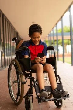Happy disabled schoolboy using mobile phone in corridor Foto stock
