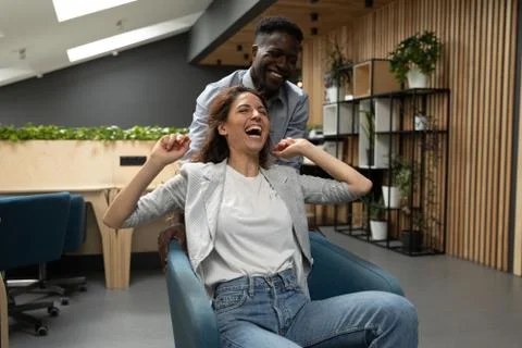 Happy diverse colleagues laughing riding on chair in office Stock Photos