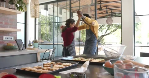 Happy diverse couple in aprons baking cookies and dancing in sunny kitchen, copy Stock Footage 338325220