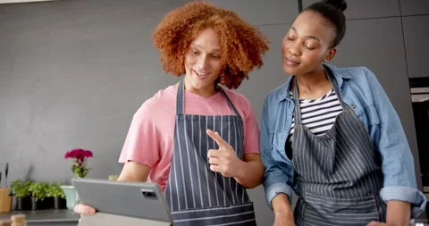 Happy diverse couple in aprons preparing vegetables and using tablet in kitchen, Stock Footage 341735904