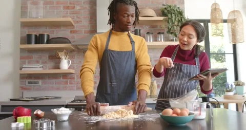Happy diverse couple in aprons using tablet and baking in kitchen, slow motion Stock Footage 341942448