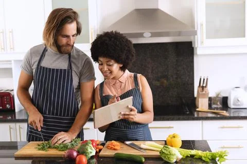 Happy diverse couple in kitchen using tablet and preparing food Fotos Stock