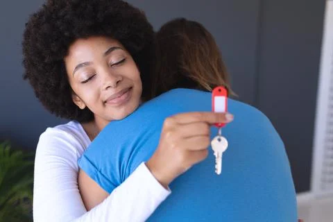 Happy diverse couple moving house smiling and embracing a woman holding key Stock Photos