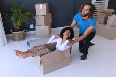 Happy diverse couple moving house smiling and playing with cartons Stock Photos