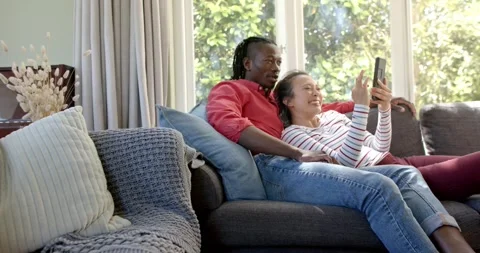 Happy diverse couple relaxing on couch using tablet in living room, copy space, Stock Footage 344333003
