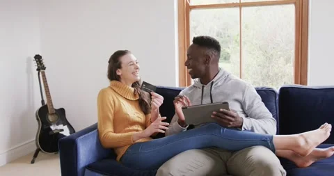 Happy diverse couple sitting on sofa, using tablet and credit card in home,copy Stock Footage 340979553