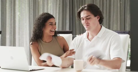 Happy diverse couple sitting at table, using laptop and shredding documents in Stock Footage 317367670