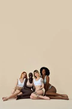 Happy multicultural girls wearing underwear standing on beige