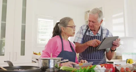 Happy diverse senior couple using tablet and cooking in kitchen Stock Footage 339320131