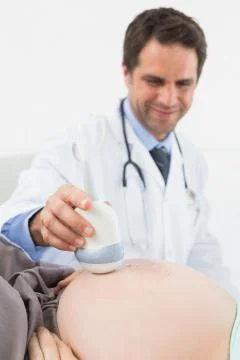 Happy doctor doing a sonogram scan on pregnant woman Stock Photos