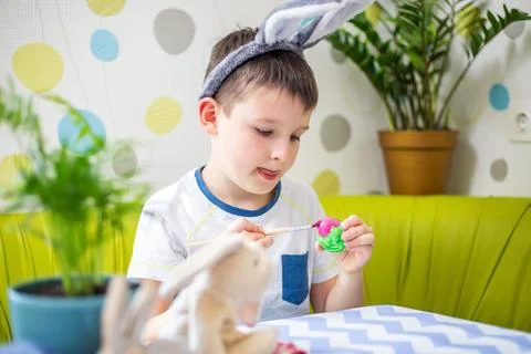 Happy Easter. Boy in bunny ears dyes colorful egg for Easter hunt Stock Photos