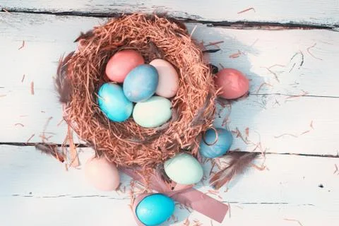 Happy Easter. Colorful Easters eggs in a nest with feathers on the wooden Stock Photos