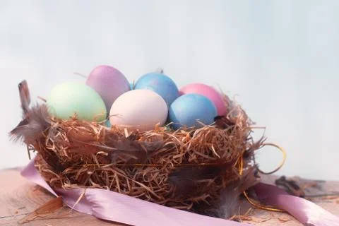 Happy Easter. Colorful Easters eggs in a nest with feathers and a chalk board on Stock Photos