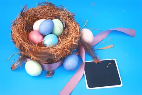 Happy Easter. Colorful Easters eggs in a nest with feathers and a chalk board on Stock Photos
