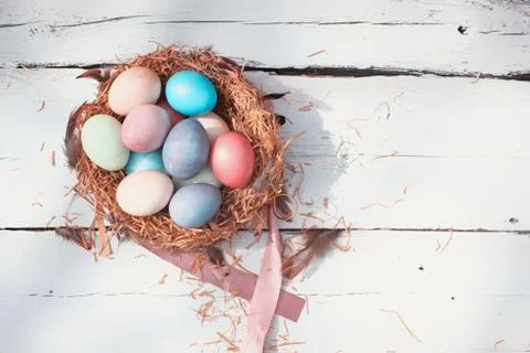 Happy Easter. Colorful Easters eggs in a nest with feathers on the wooden Stock Photos