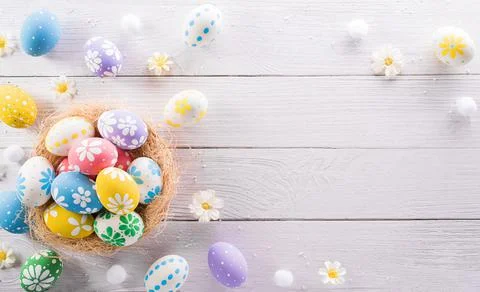 Happy easter! colourful Easter eggs in a nest with flower on white wooden bac Stock Photos