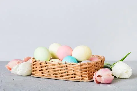 Happy Easter composition. Easter eggs in basket on colored table with yellow  Stock Photos