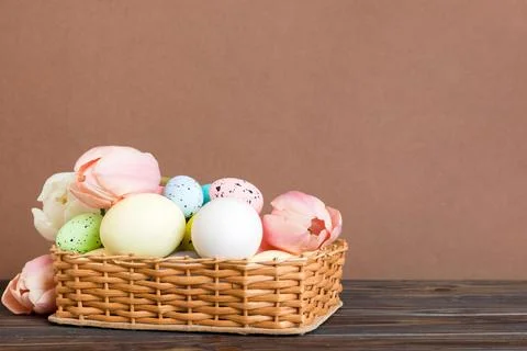 Happy Easter composition. Easter eggs in basket on colored table with yellow  Stock Photos