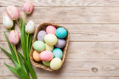 Happy Easter composition. Easter eggs in basket on colored table with yellow  Stock Photos