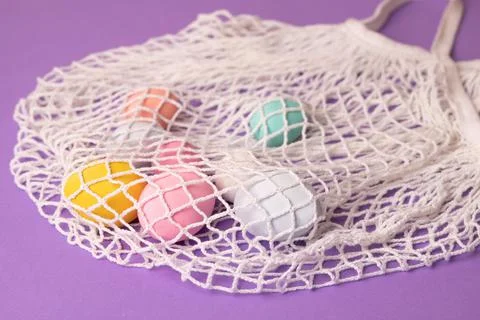 Happy Easter concept with assorted pastel eggs in a knitted mesh shopping bag Stock Photos