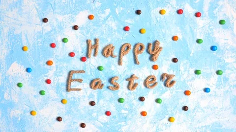 Happy Easter congratulation and moving dragee on blue background, stop motion. Stock Footage 123904009