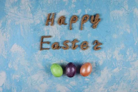 Happy Easter congratulation and three colorful eggs on the blue background. Stock Photos