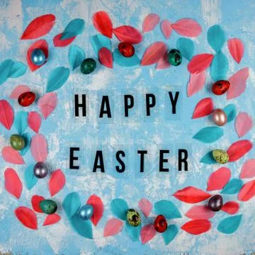 Happy Easter congratulation on the blue background among feathers and colored Stock Photos