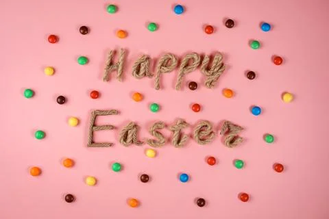 Happy Easter congratulation on the pink background among colorful dragee. Stock Photos