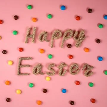 Happy Easter congratulation on the pink background among colorful dragee. Stock Photos