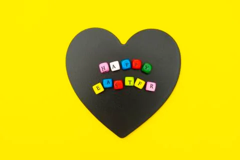 Happy Easter. Cubes with text on heart shaped blackboard, yellow background.  Stock Photos