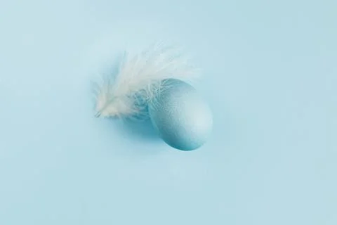 Happy Easter! Easter egg and feather on blue background flat lay. Minimal E.. Stock Photos
