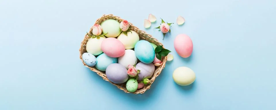 Happy Easter. Easter eggs in basket on colored table with yellow roses. Natur Stock Photos