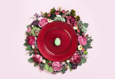 Happy Easter egg on red plate on floral wreath flat lay Stock Photos