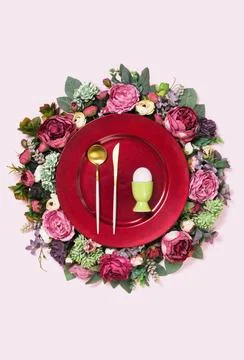Happy Easter egg on red plate on floral wreath flat lay Stock Photos