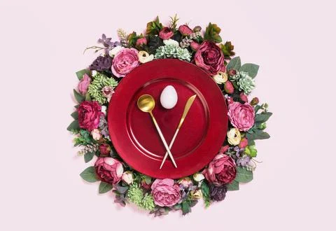 Happy Easter egg on red plate on floral wreath flat lay Stock Photos