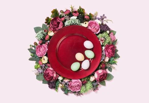 Happy Easter eggs on red plate on floral wreath flat lay Stock Photos