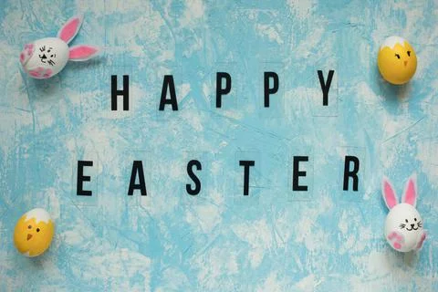 Happy Easter greeting on sky blue textured background among funny Easter eggs Stock Photos