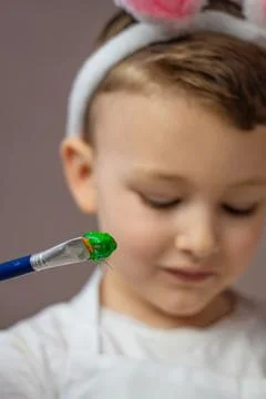Happy Easter, kid. Boy in rabbit ears paint eggs in the kitchen of the house 스톡 사진