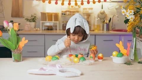 Happy Easter, kid. Girl in rabbit ears paint eggs in the kitchen of the house Stock Footage 149987049