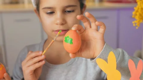 Happy Easter, kid. Girl in rabbit ears paint eggs close up in the kitchen of the Stock Footage 149987089