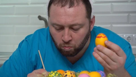 Happy Easter. A man in a rabbit ears blue t-shirt in the kitchen paints eggs Stock Footage 124857817