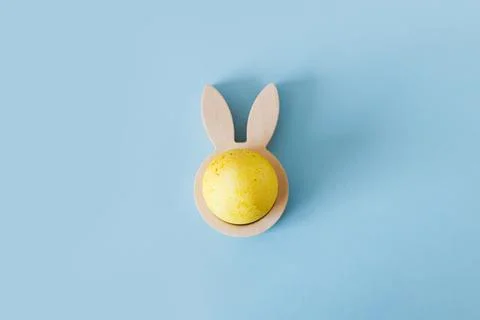 Happy Easter! Modern yellow easter egg in wooden bunny ears holder flat lay.. Stock Photos